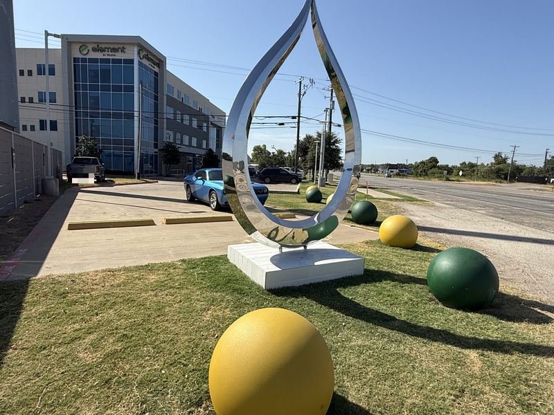 The mirror-polished stainless steel teardrop sculpture with green and gold spheres at the Waco Traffic Circle